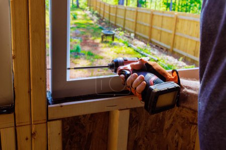 Bauarbeiter baut Kunststofffenster mit Schraubenzieher in neuem Wohnhaus ein