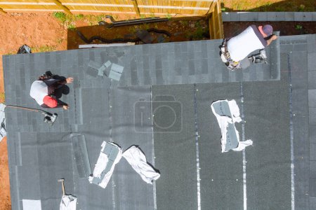 Un entrepreneur de toiture expérimenté utilise un pistolet à ongles d'air pour installer de nouveaux bardeaux de bitume d'asphalte sur le toit de la maison