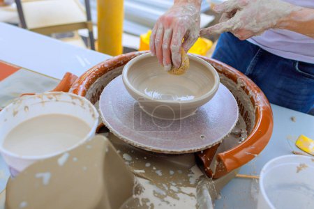 Using wet hands, ceramicist shapes soft clay on potter wheel