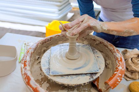 In potter is sculpting soft clay with wet hands while making clay dishes on potter wheel