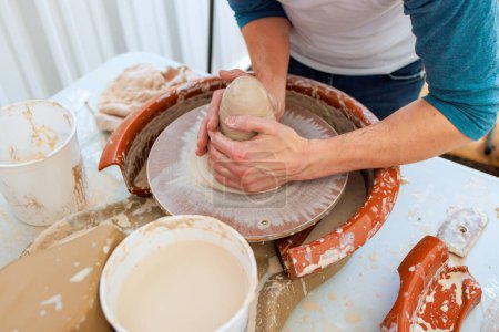In potter wheel, wet hands sculpt soft clay as potter creates clay dishes