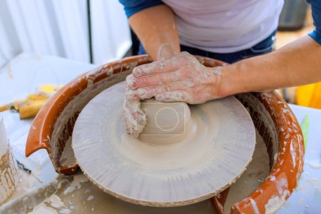 An artist makes clay dishes using wet hands on potter wheel