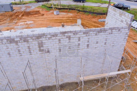 Téléchargez les photos : Travailleur de la construction debout sur l'échafaudage fait mur de béton de travail à partir de blocs de béton - en image libre de droit