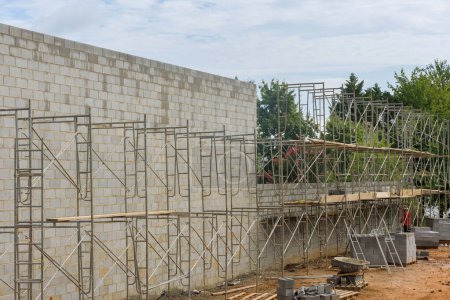 On scaffolding, bricklayer builds concrete wall from concrete blocks