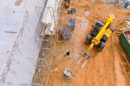 Téléchargez les photos : Constructeur de maçon font mur de béton de travail à partir de blocs de béton debout sur des échafaudages - en image libre de droit