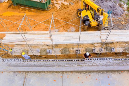 Téléchargez les photos : Bricklayer construit mur de béton de travail à partir de blocs de béton tout en se tenant debout sur échafaudage - en image libre de droit