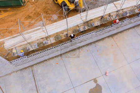 En el sitio de construcción, albañil hace muro de hormigón utilizando bloques de cemento mientras está de pie en andamios