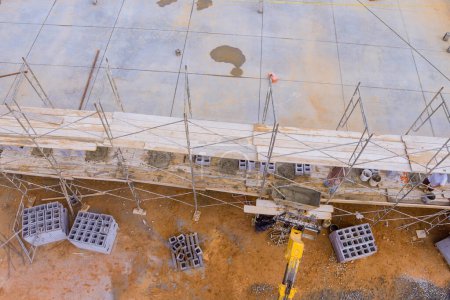 Trabajador de mampostería se para en andamios mientras hace muro de hormigón utilizando bloques de cemento