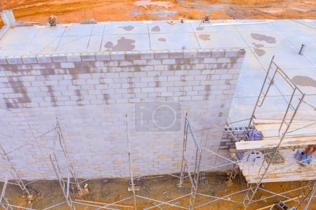 En el sitio de construcción, albañil hace paredes de hormigón con bloques de cemento mientras está de pie sobre andamios