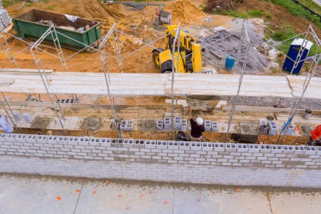 En el sitio de construcción, los puestos de albañilería sobre andamios construyen muros de hormigón utilizando bloques de cemento
