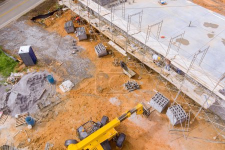 Trabajador de mampostería hacer muro de hormigón por bloque de cemento de pie en andamios en el sitio de construcción