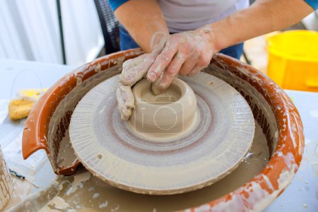 Worker creating bowl with wet soft clay using potter wheel