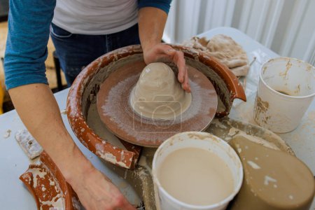 Working with wet soft clay on potter wheel, professional potter creates bowl