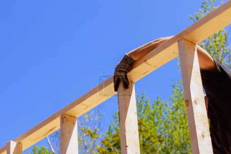 As framer installs beams using an air nail hammer, he nails wooden planks to frame