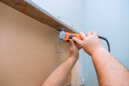 An employee cuts drywall with multi tool in wall