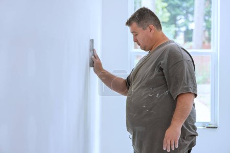 Worker sanding plasterboard walls after they have been puttied