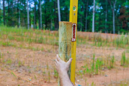 Man building wooden fence in backyard checking posts with level