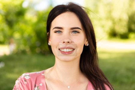 Foto de Close up head portrait of smiling caucasian woman with white teeth looking at the camera. Perfect healthy smile with veneer. Skin and dental care. Nature green background. - Imagen libre de derechos
