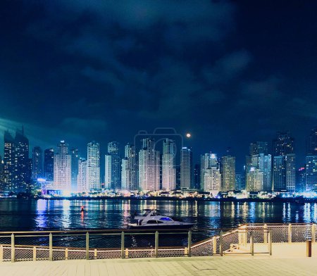 Photo for Evening marine view from Dubai Bluewaters promenade to Jumeira Beach residence, boat floating at water and moon under skyscrapers - Royalty Free Image