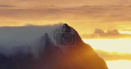 This image captures the breathtaking moment when sharp mountain peaks emerge above a dense sea of clouds as the sun sets in the background. High quality 4k footage