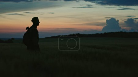 Soldier in uniform silhouetted against the sunset walking towards the camera across open countryside.