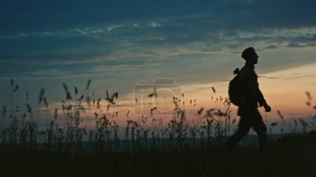 Soldat in Uniform vor Sonnenuntergang, der auf offener Landschaft auf die Kamera zugeht.