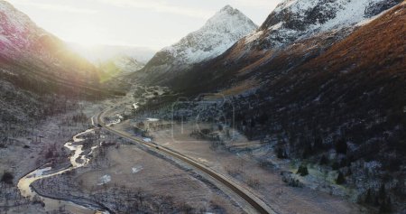 Sunlit Peaks and Winding River: Aerial View of a Norwegian Valley. E10 Road Through Snowy Peaks: Aerial View of Lofotens Winter Landscape. High quality 4k footage