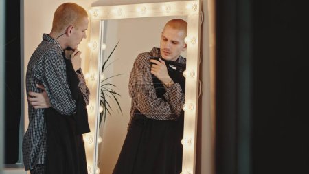 Young Man at Illuminated Mirror Trying on a Dress, Exploring Gender Identity. High quality 4k footage