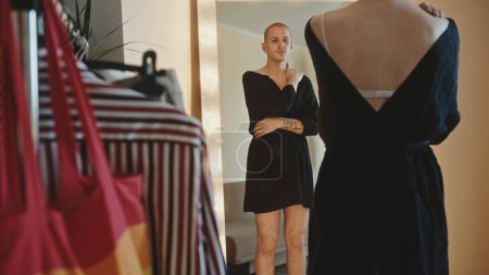 Un mec à la maison, gay, debout près d'un miroir éclairé portant une robe de femme et regardant dans le miroir. Images 4k de haute qualité