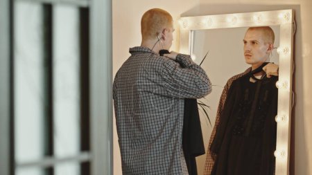 Jeune homme gay à la maison essayant une robe par un miroir lumineux. Images 4k de haute qualité