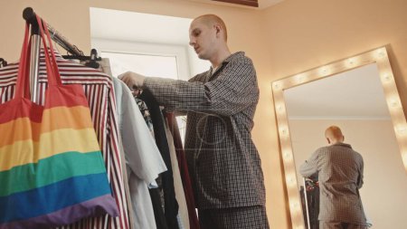 Attractive transgender man trying on female shirt and looking at mirror at home. High quality 4k footage