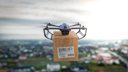 Téléchargez les photos : Le drone vole au-dessus de la ville avec un paquet pour le client - une vue rapprochée de l'appareil, le concept de livraison de drones. - en image libre de droit