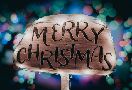 Téléchargez les photos : Joyeux Noël signe en bois illuminé avec des lumières de vacances sur fond d'arbres de Noël ornés de lumières festives - en image libre de droit