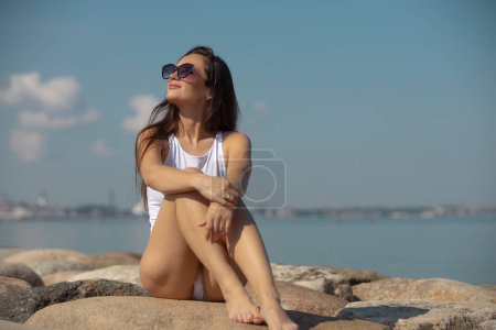 Téléchargez les photos : Young beautiful woman in a white swimsuit against the sky - en image libre de droit
