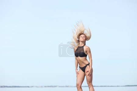Téléchargez les photos : Jeune femme en maillot de bain noir sur la plage - en image libre de droit