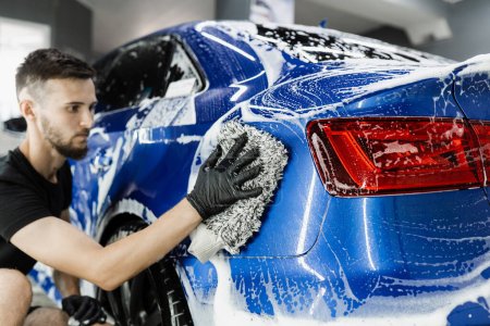 Autowaschanlage beim manuellen Schaumwaschen im Auto-Detaillierungsservice. Händewaschen mit Mikrofaserhandschuh mit Schaumstoffkarosserie in der Garage