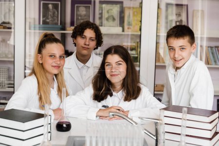Foto de School education. Cheerful classmates in chemistry lesson hold flasks with liquid for experiments. Happy friends study together in class in laboratory - Imagen libre de derechos