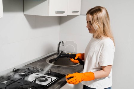 Woman housekeeper is steaming on cooker using steam generator. Steam cleaning of cooker in kitchen. Professional domestic cleaning service
