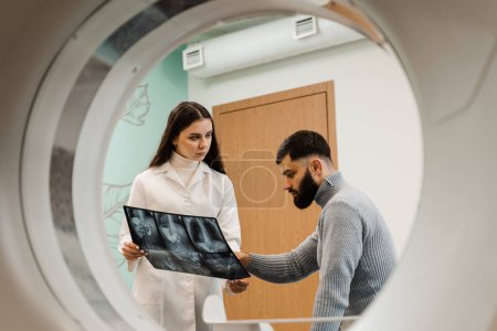 Foto de CT scan radiologist showing x-ray of abdomen to man patient in computed scanning room. CT Doctor consulting patient and showing chest x-ray to patient in computed tomography room - Imagen libre de derechos