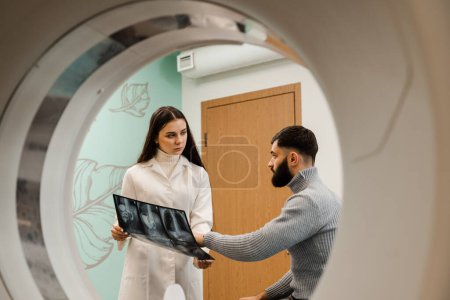Foto de CT Doctor consulting patient and showing chest x-ray to patient in computed tomography room. CT scan radiologist showing x-ray of abdomen to man patient in computed scanning room - Imagen libre de derechos