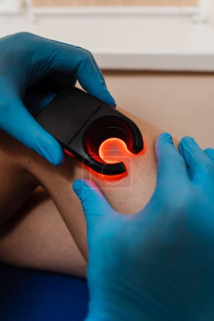Photo for Vascular surgeon examines leg veins of woman using led venous scanner with red illumination. Venous led scanner for helping to locate the veins - Royalty Free Image