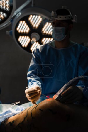 Photo for Vascular surgeon is operating leg using EVLT Red laser optical fiber for endovenous laser coagulation for treatment varicose veins, thrombophlebitis, thrombosis of legs in operating room - Royalty Free Image