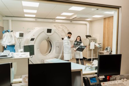 Foto de Doctores discutiendo radiografías en la sala de tomografía computarizada. Médico médico interno chica está estudiando en la sala de exploración por tomografía computarizada CT en cursos de prácticas - Imagen libre de derechos