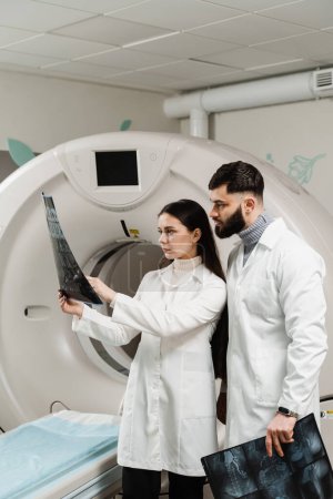 Foto de Los doctores de la tomografía computarizada están discutiendo la radiografía de la tomografía computarizada del cerebro del paciente. Los médicos de tomografía computarizada están consultando y discutiendo la radiografía del paciente - Imagen libre de derechos