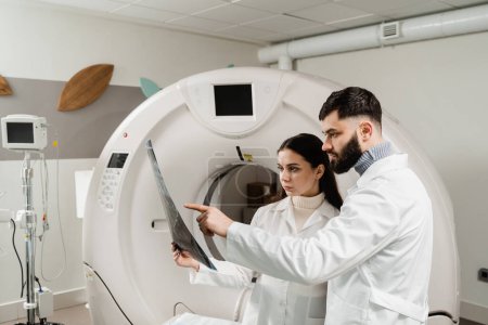 Foto de CT Computed tomography scan procedure to obtain detailed internal images of body and research on tumors in head, brain, and spine. Two doctors discussing x-rays after CT scan of patient abdomen - Imagen libre de derechos