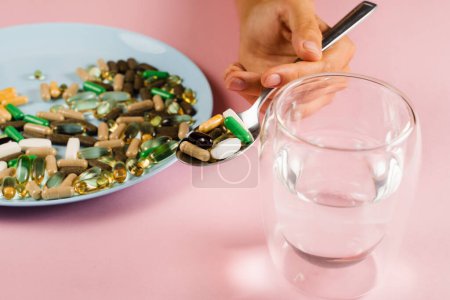 Téléchargez les photos : Many dietary supplements tablets, glass of water and spoon for daily pills intake on pink background. Set of mulvitamin, amino acids, minerals and magnesium antistress, melatonin close-up - en image libre de droit