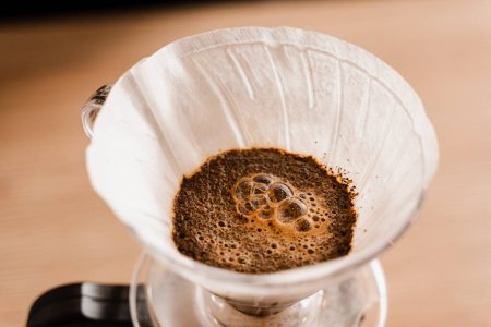 Photo for Pour over filter with ground coffee in the funnel in focus. Drip filter coffee brewing. Pour over alternative method of pouring water over roasted and ground coffee beans contained in filter - Royalty Free Image