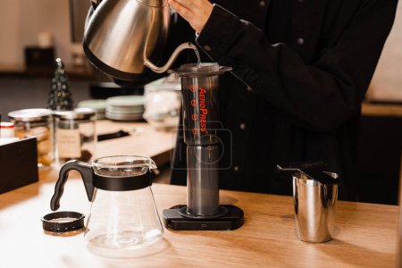 Barista brüht im Café Aeropress-Kaffee. Prozess der Aeropress alternative Methode Kaffee brauen. Heißes Wasser über geröstete und gemahlene Kaffeebohnen in der Aeropress gießen