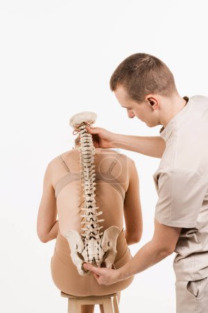 Photo for Orthopedist showing spinal column model with girl on white background. Scoliosis is sideways curvature of the spine. Backbone anatomical model with young woman - Royalty Free Image