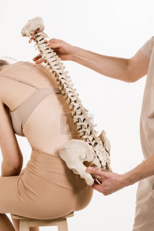 Photo for Orthopedist showing spinal column model with girl on white background. Scoliosis is sideways curvature of the spine. Backbone anatomical model with young woman - Royalty Free Image